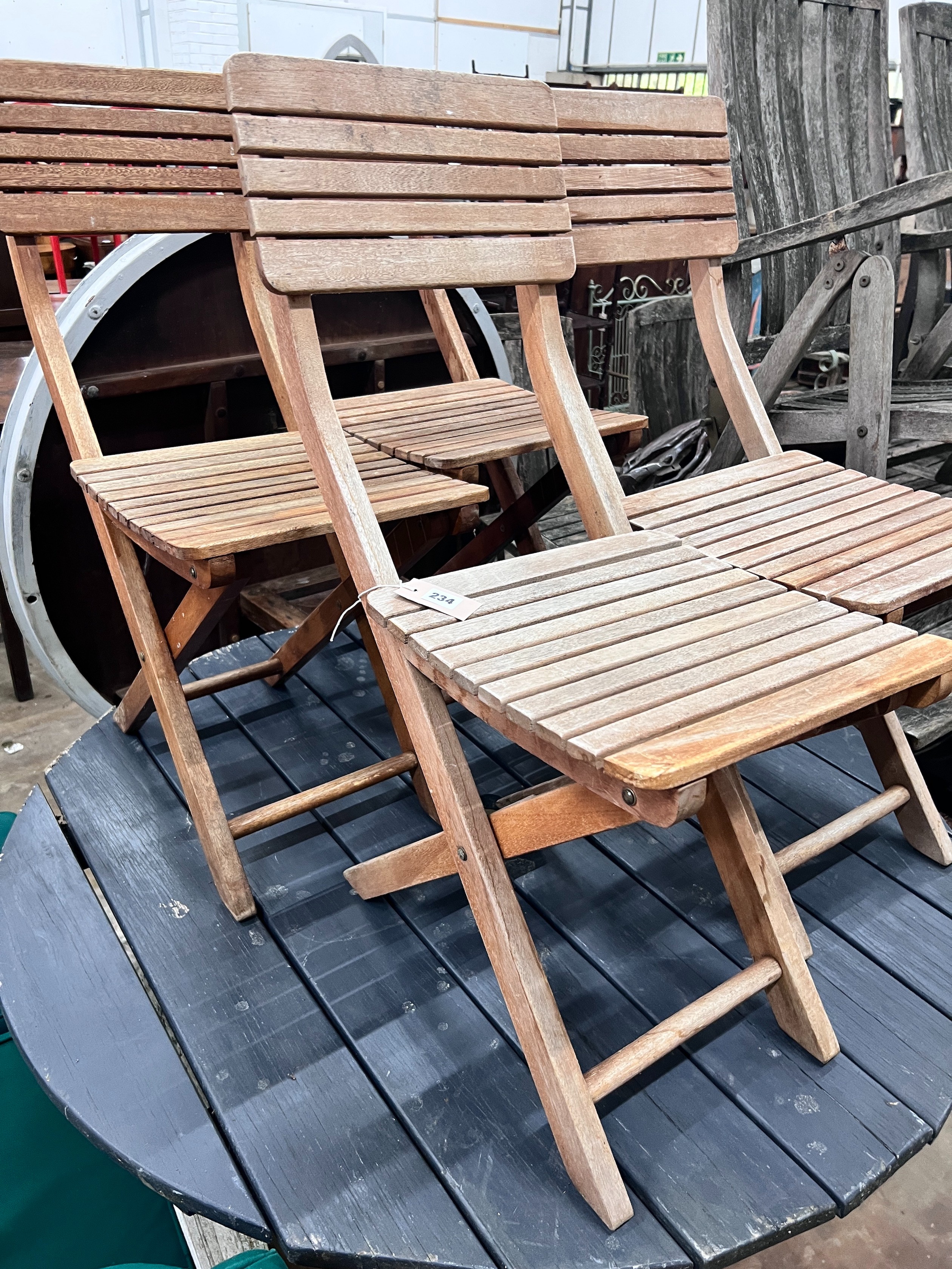 A grey stained teak circular garden table and four faded teak folding chairs, table diameter 120cm *Please note the sale commences at 9am.